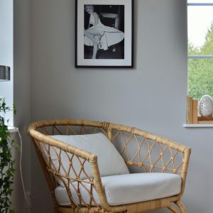 A stylish wicker chair in a Scandinavian-designed room with a framed photo on the wall.